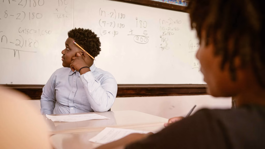Two students seated at a table looking up at the board